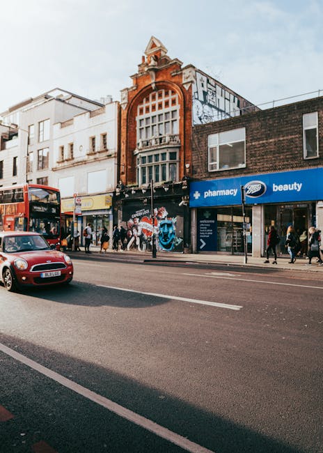 An exterior view of a commercial street in Putney featuring a historic brick building with large arched windows and decorative elements at the top, surrounded by modern shops including a pharmacy and 