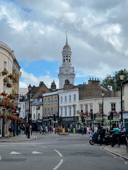 An exterior view of a commercial street in Putney featuring a historic brick building with large arched windows and decorative elements at the top, surrounded by modern shops including a pharmacy and 